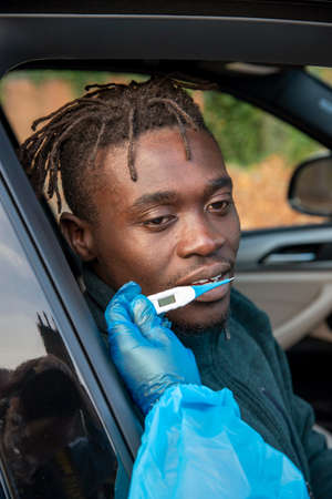 Southern England, UK. 2020.  Black client at Covid-19 testing centre having temperature taken.の写真素材