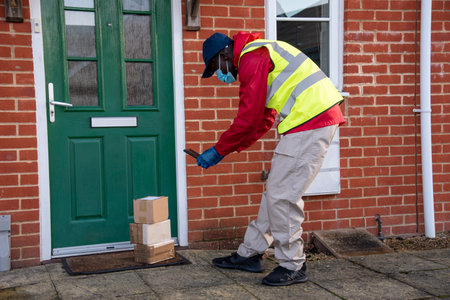 Hampshire, England, UK. 2020, Male courier delivering parcels and packages during Covid-19 epidemic...