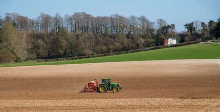 Hampshire, England, UK. 2021. Spring and a green tractor with a seed drill working in  a field at Micheldever near Winchester, England, UKのeditorial素材