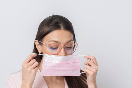 Salisbury, Wiltshire,UK. 2021. Woman wearing glasses placing a pink coloured medical mask on her face during covid.の写真素材