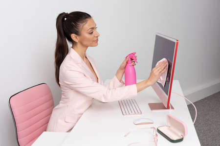 Wiltshire, England, UK. 2021.  Woman at desk using a spay bottle and cloth to clean and sanitise a...