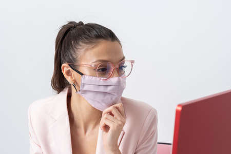 Salisbury, Wiltshire, UK. 2021. Attractive woman wearing pink facemask and using a computer and keyboard.の写真素材