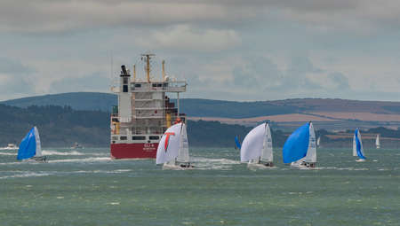 Solent, southern England, UK. 2022. Cowes week and racing yachts close to the container carrier ship Eli A on the Solent with a backdrop if the Isle of Wight coastline.の写真素材