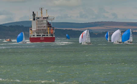 Solent, southern England, UK. 2022. Cowes week and racing yachts close to the container carrier ship Eli A on the Solent with a backdrop if the Isle of Wight coastline.の写真素材