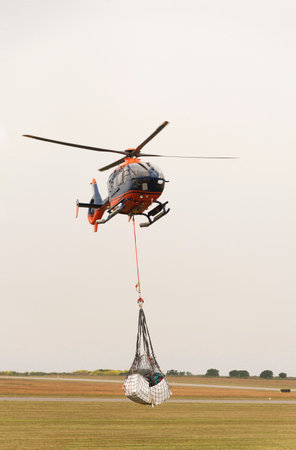 Cornwall, England, UK. 2022. Airlift helicopter with carrying strap and netting cargo carrier above a Cornish airfield on a collection and delivery operation.のeditorial素材