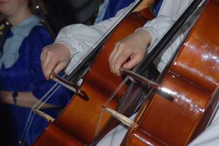closeup of two people playing cellos in time during a live performanceの写真素材