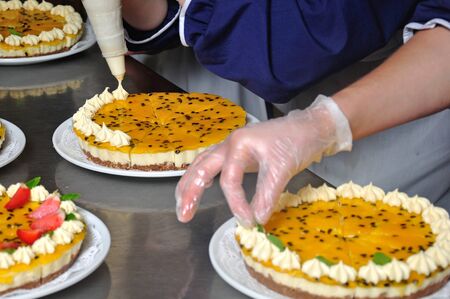 cook placing cream on the top of a passionfruit cheesecakeの写真素材