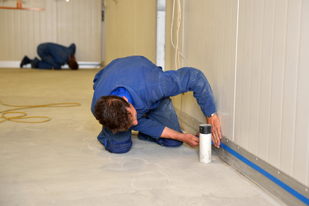 tradesman masks off the height of the coving before applying epoxy product to the floor of an industrial buildingの写真素材