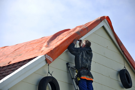 GREYMOUTH, NEW ZEALAND, APRIL 17, 2014: Volunteer worker places a tarpaulin on a house de-roofed in Cobden by Cyclone Ita, Greymouth, New Zealand, April 17, 2014のeditorial素材