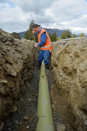 A tradesman packs gravel under a pipe in a new stormwater drainの写真素材