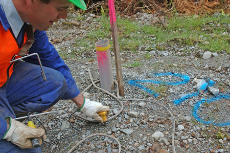 Man places geophone in ground at hole 210 for seismic test, Westland, New Zealand