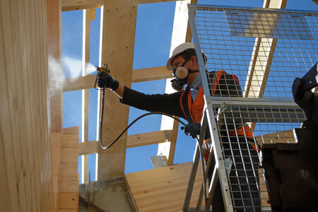 Tradesman spray painting the wall of a wooden industrial building with timber preservativeの写真素材