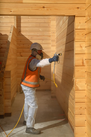 Tradesman spray painting the wall of a wooden industrial building with timber preservativeの写真素材