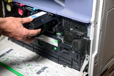 An office worker replaces a black toner cartridge in a photocopier