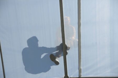 GREYMOUTH, NEW ZEALAND, DECEMBER 12, 2018: A tradesman in seen in silhouette as he secures the plastic on the ridge of a tunnel house.のeditorial素材