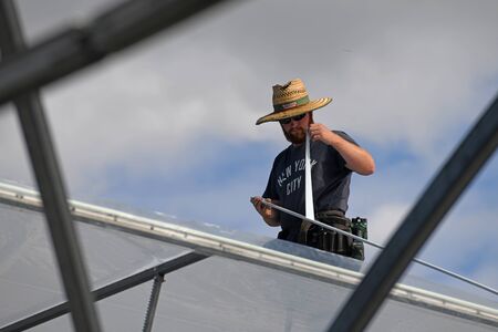 GREYMOUTH, NEW ZEALAND, DECEMBER 12, 2018: Tradesmen secure the plastic on a new tunnel house.のeditorial素材