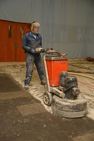 WEST COAST, NEW ZEALAND, JUNE 28, 2019: A tradesman uses a grinding machine to remove old carpet squares from a floor in preparation for new floor coverings.のeditorial素材
