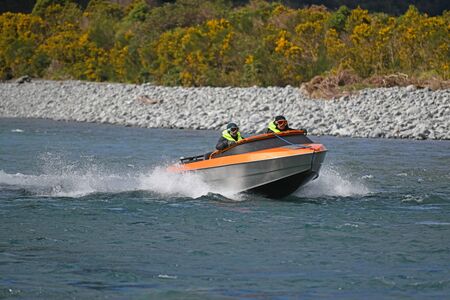 TARAMAKAU RIVER, WEST COAST, NEW ZEALAND, SEPTEMBER 3, 2019: Two people power their jetboat down the...