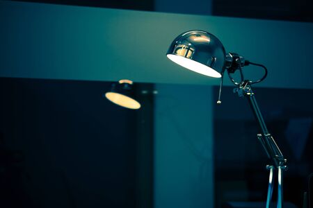 Compact Desktop Lamp Photo with Copy Space. Working at Night Concept. Dark Bluish Color Grading.の写真素材