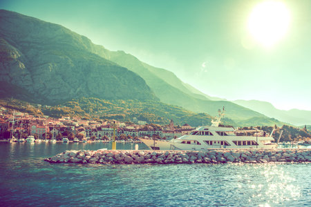 Scenic View of Croatian Tourist Town on Sunny Summer Day. Clear Blue Water, Modern Yacht, Cottages with Red Roods on the Shore. Huge Mountain in the Background. Traveling and Tourism Theme.の写真素材