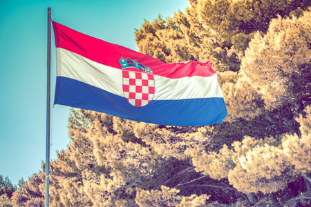 Closeup of Waving National Flag of Croatia. Blue Sky and Large Trees in the Background. Traveling and Countries and Cultures Exploring Theme.の写真素材