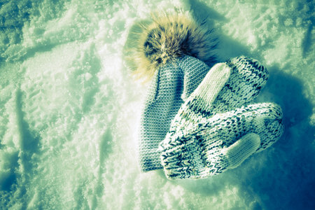 Winter Hat and Gloves Lying on Snowy Background in Artificial Evening Light. Lost and Found Things. Warming Clothes and Accessories.の写真素材