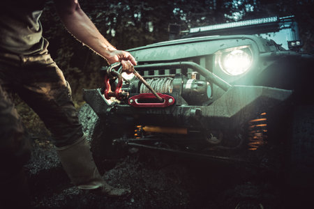 Off-Road Vehicle Got Stuck in the Mud During Recreational Ride. Driver Assistant Unrolling the Winch to Help Pull the Car Out. Muddling in the Forrest.の写真素材