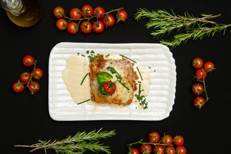 Lasagne with basil leafs in white dish. Classic italian dish. Tomatoes and rosemary on the table. Italian cuisine.の写真素材