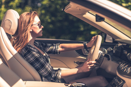 A fulfilled young woman driving a convertible during sunset. Wind in hairs.の写真素材