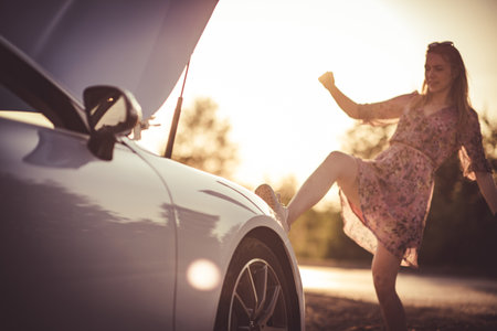 Woman kicking her broken car. Sunset.の写真素材