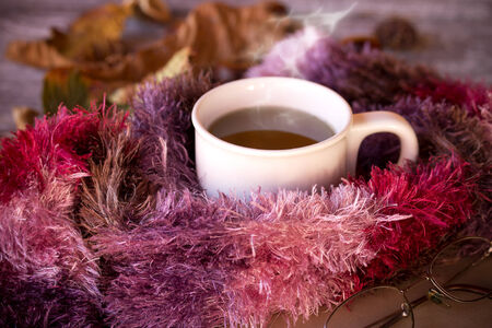Cup of hot tea dressed in knitted warm winter scarf on brown wooden tabletopの写真素材