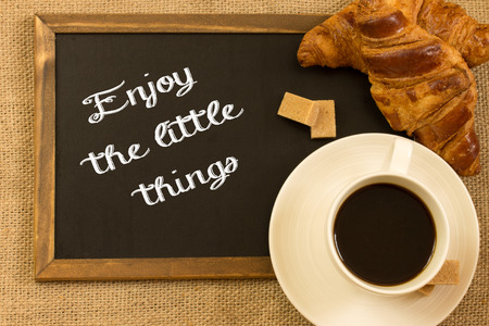 Inspirational early morning breakfast of a croissant with fresh filter coffee and a note handwritten - Enjoy the little thingsの写真素材