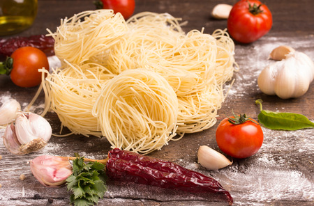 Italian pasta fettuccine nest, cherry tomato, parsley, garlic on wooden tableの写真素材