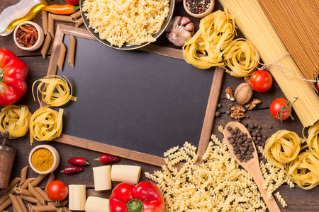 Italian pastas and food ingredients on vintage wood background, with chalkboard, with copyspaceの写真素材