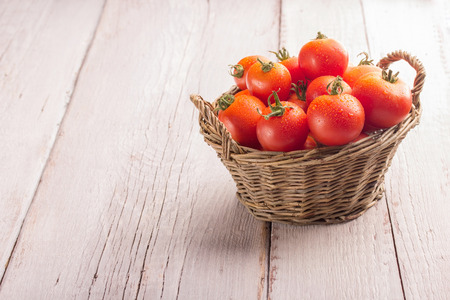 tomatoes in a cute basket on a white wooden tableの写真素材