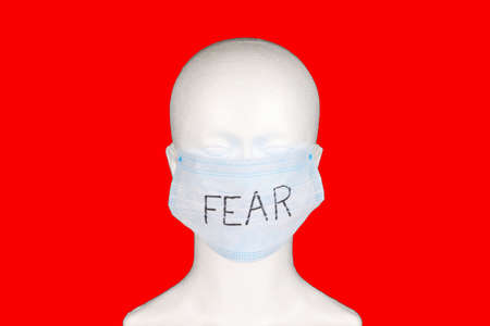 fear written on a face mask placed on a mannequin dummy with red backgroundの写真素材