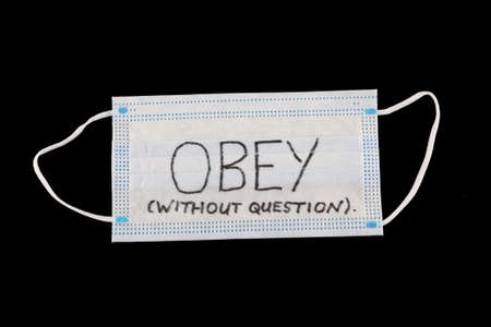 obey without question drawn on a face mask against black backgroundの写真素材