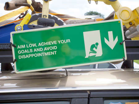 sardonic bittersweet green sign stating aim low, achieve your goals and avoid disappointment.の写真素材
