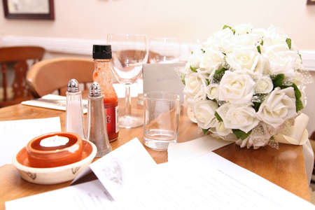 white rose wedding flowers sat on a table with glasses and condimentsの写真素材
