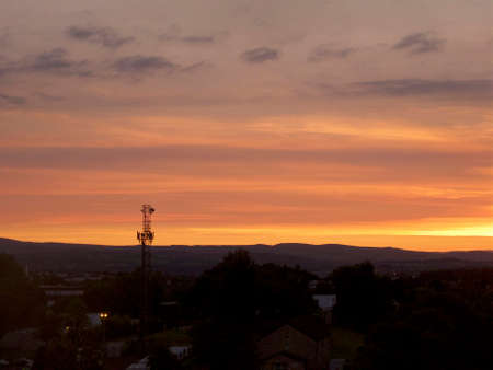 sun setting over the hills with tv antenna and hills silhouetted against an orange and yellow cloudy skyの写真素材