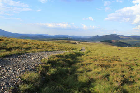 path in the hillside of the scottish highlands with hills and cloudy blue skies in view.の写真素材