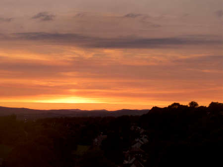 sun setting over a silhouetted landscape with orange cloudy skyの写真素材