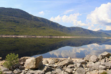 crocodile shaped hillside reflecting on the river with still water, rocks and cloudy blue skies in the picture.の写真素材