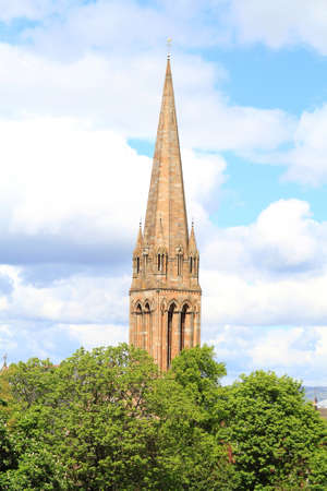 spire of a church in the south side of glasgow showing through the trees in summer time with white fluffy clouds and blue skies on the horizon.の写真素材