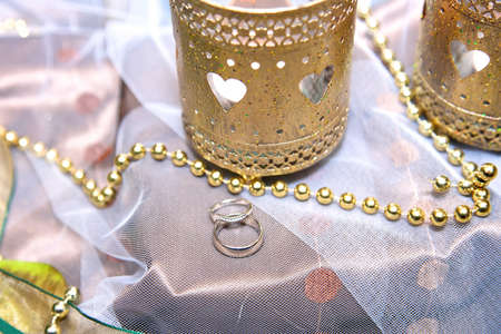 silver wedding rings with gold pearls and candles placed on a silk cover.の写真素材