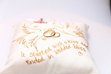 two gold wedding rings sat on a cushion with inscription and two dovesの写真素材