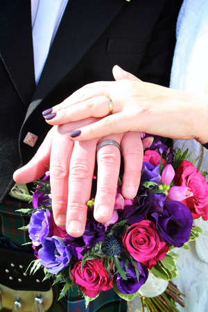 bride and groom hands showing their wedding rings sat atop a bouquet of brightly coloured flowers on a sunny day.の写真素材