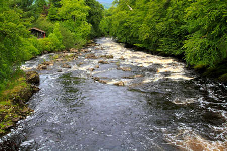 wide angle view of the meandering river with trees on either side and wooden hut in view.