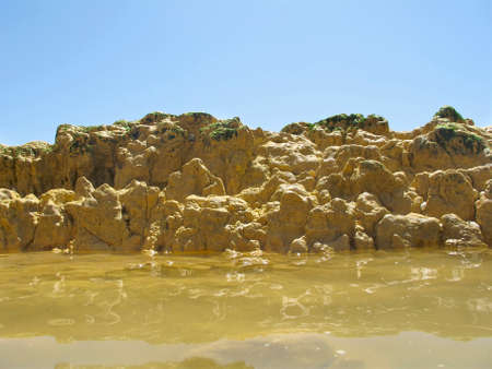 rock pool with yellow coloured sea water and clear blue sky in the background.の写真素材