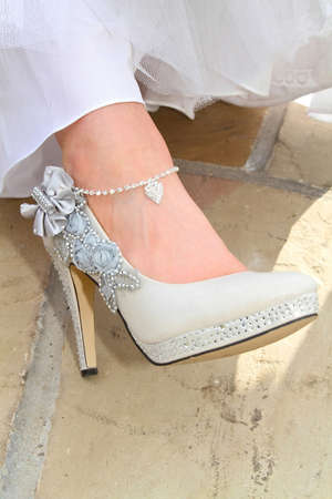 cream coloured brides shoe with ankle bracelet with the bottom of the wedding dress in view.の写真素材